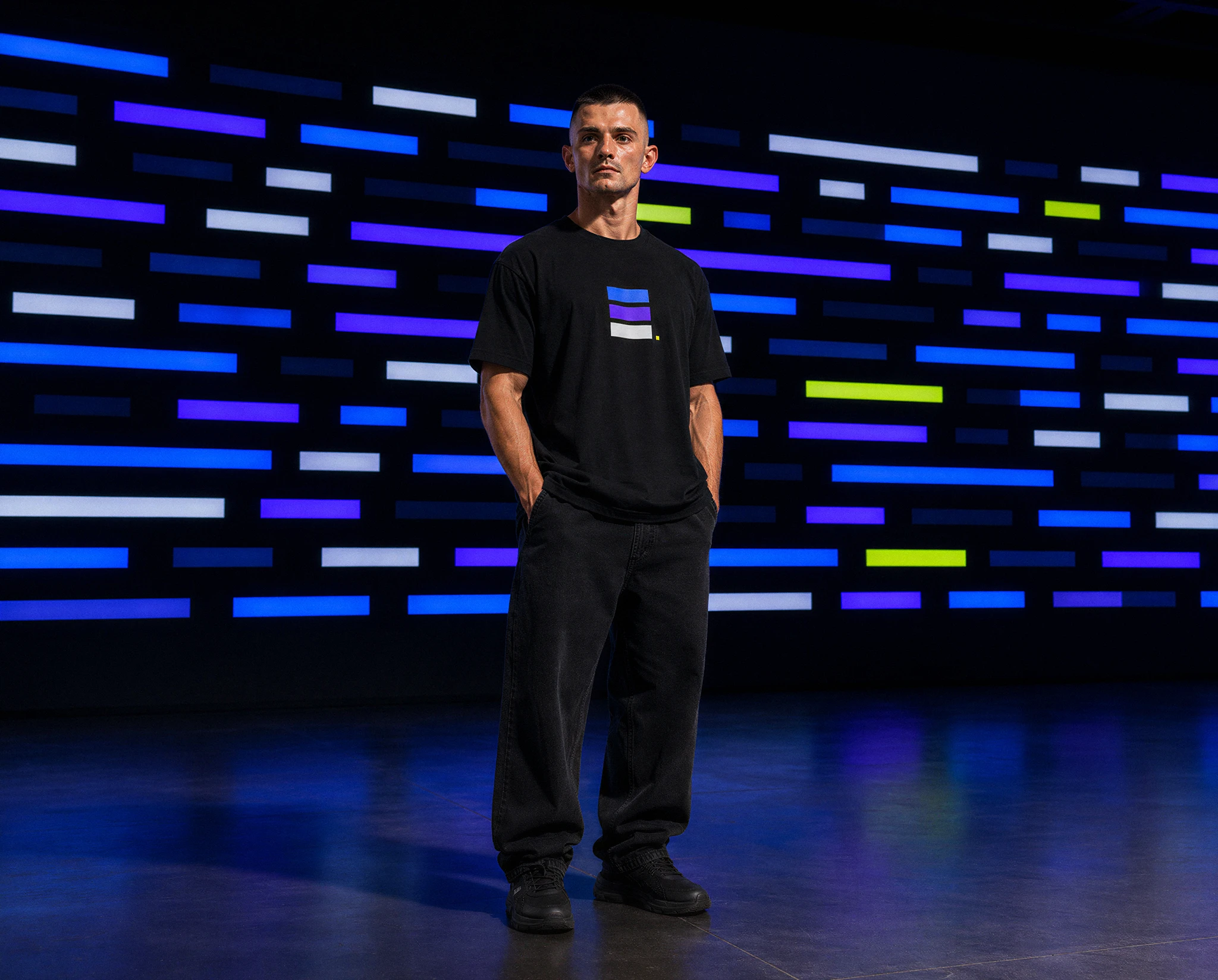 Man in black GRAPHIC T-shirt standing before a large luminous screen of blue, violet, grey and chartreuse rectangles in a dark performance space — synthographic artwork by davidname.