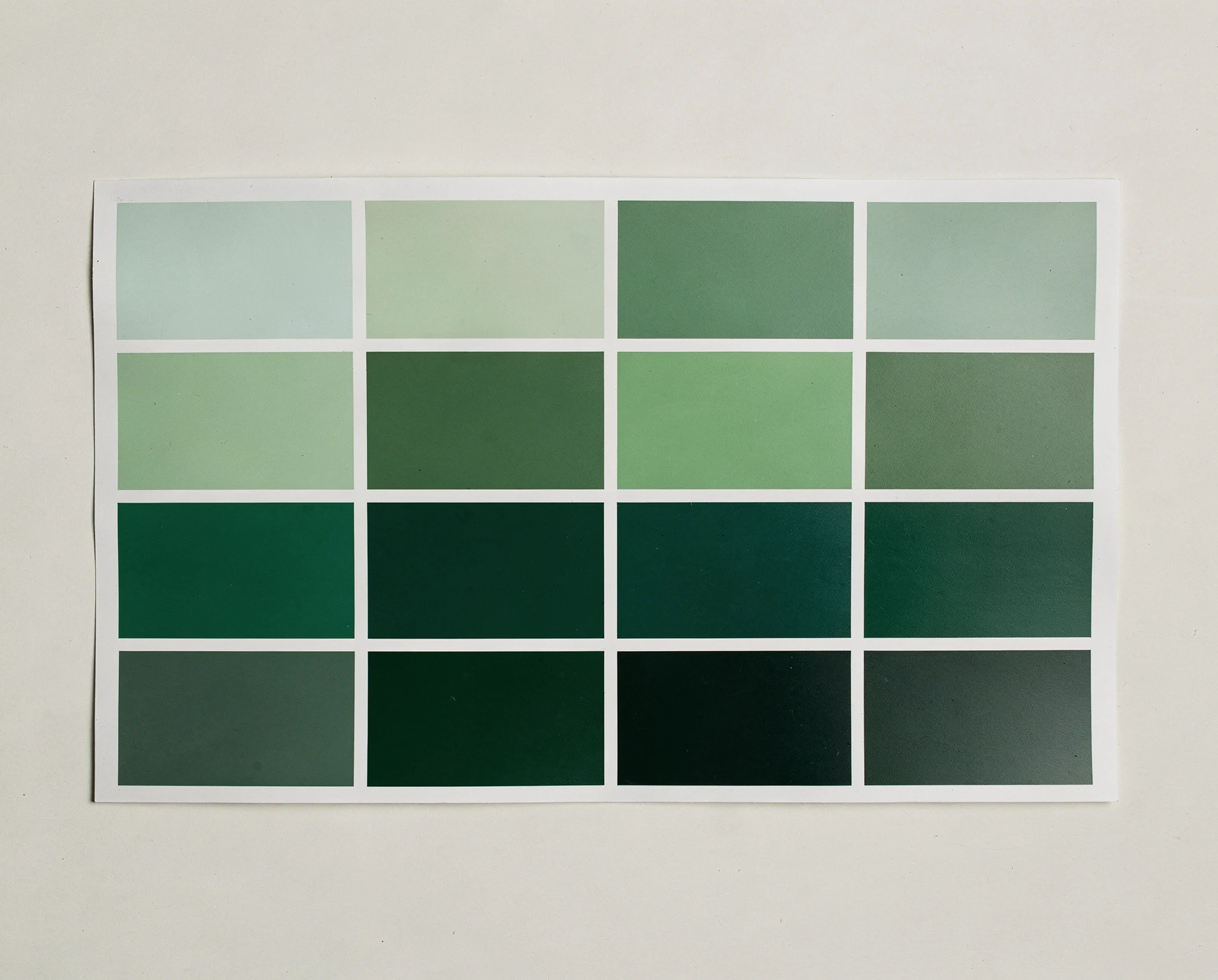 Photographed printed colour chart showing a grid of green paint swatches on a pale background — synthographic artwork by davidname.